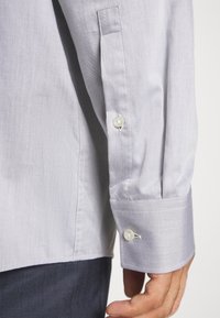 Light blue shirt sleeve made from textured fabric. Features a button closure with a white button and a crisp cuff.
