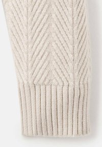 Manga de suéter de punto en un tono beige claro, con un patrón en espiga texturizado y puño acanalado para mayor detalle y estructura.