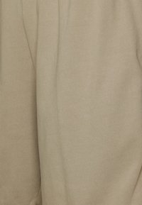 Tejido de punto beige con una textura suave, que presenta un sutil patrón acanalado. El material parece blando y ligeramente elástico.