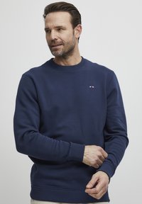 Maglione blu navy realizzato in tessuto misto cotone, con colletto tondo, polsini a costine e un piccolo dettaglio del logo sul petto.