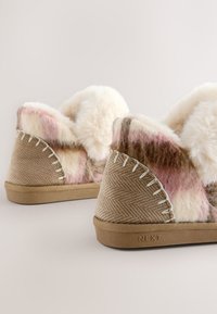 Chaussons beiges et roses à motif, à la texture douce, avec un design en chevron et une couture blanche contrastante. Semelle en caoutchouc avec logo.