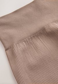 Ribbade leggings i ett varmt taupe-färgat tyg, med bred resår i midjan och mjuk textur med vertikala ribbmönster för extra detalj.