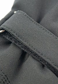 Guante de tela negra con textura suave, costuras reforzadas y una correa de Velcro para un cierre seguro. Vista en primer plano del detalle de la costura.