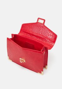 Sac en cuir embossé crocodile rouge avec une surface texturée, des ferrures en or et un rabat ouvert révélant un intérieur rouge lisse.