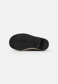Suela de zapato de goma negra con un patrón en zigzag, una superficie texturizada y un borde beige. Marca sutil grabada cerca del área de los dedos.