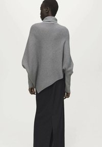 Poncho grigio a coste in maglia con collo alto, orlo asimmetrico e vestibilità rilassata, abbinato a una lunga gonna nera con spacco laterale.