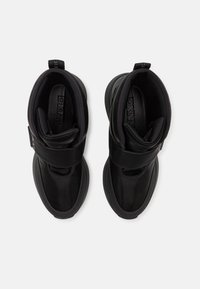 Høye svarte sneakers med borrelås og polstrede ankelkrager, sett ovenfra på en hvit bakgrunn.