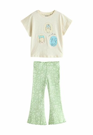 Camiseta de algodón en color crema con caras de dibujos animados y texto; combinada con pantalones acampanados verdes con pequeños patrones florales blancos.