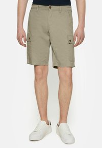 Khaki cargo shorts, joissa on kaksi sivutaskua, nappilistans sulku ja rento istuvuus. Yhdistetty valkoisiin lenkkareihin kontrastiksi.