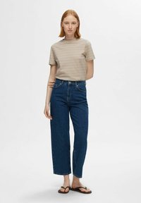 Camiseta de manga corta a rayas beige combinada con jeans de pierna recta de tiro alto en azul oscuro y chanclas marrones. Diseño minimalista y colores clásicos.