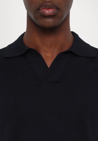 Polo azul-marinho com um tecido suave e texturizado, apresentando um colarinho clássico e um leve design em V.