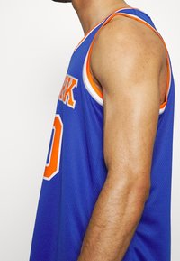 Niebieski T-shirt koszykarski z pomarańczowymi akcentami i tekstem. Siatkowy materiał, bez rękawów, z wyraźnym numerem "0" na przodzie.