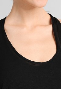 Czarny top bez rękawów z szerokim, zaokrąglonym dekoltem, wykonany z lekkiego materiału, o delikatnej fakturze i luźnym kroju.