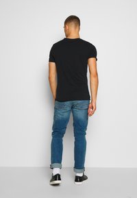 Camiseta negra de manga corta combinada con jeans de mezclilla azul claro, arremangados en los puños, con zapatos negros y calcetines blancos visibles.