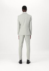 Šviesiai pilkas kostiumas su pritaikytu siluetu. Švarkas turi išpjautą apykaklę ir du mygtukus; kelnės yra siauros. Juodi batai užbaigia išvaizdą.