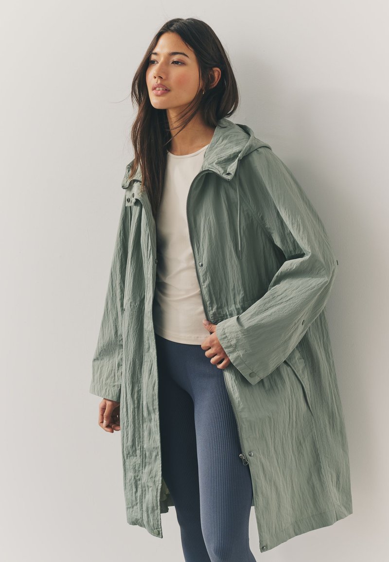 Light green, hooded jacket in a crinkled texture, featuring a front zipper and snap buttons, paired with a cream top and blue ribbed leggings.