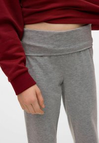 Szare dresowe spodnie z szerokim pasem, w połączeniu z bordową bluzką z długim rękawem. Materiał wydaje się miękki i ma lekki heatherowy wzór.