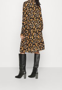 Schwarze knöchelhohe Stiefel mit einem gestapelten Absatz, kombiniert mit einem langärmeligen Kleid mit einem orangefarbenen Blumenmuster auf schwarzem Hintergrund.