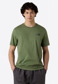 T-shirt verde oliva a maniche corte, tessuto di cotone, collo rotondo, con un logo nero sul petto a sinistra e vestibilità rilassata.