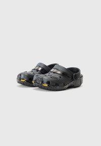 Black clogs with ventilation holes, textured surface, adjustable strap, and yellow and grey accents on the sole. Lightweight material.