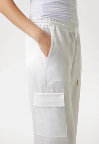 Vita satinjoggers med elastisk midjeband, sidofickor och en stor ficka med en slät textur och subtil lyster.