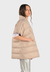 Beige oversized pufferjacka med horisontella sömmar, hög krage, korta ärmar, sidofickor och en slät, blank yta.