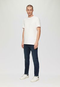 T-shirt en coton blanc à manches courtes, associé à un jean slim bleu foncé et des baskets blanches, avec une texture lisse et un design minimaliste.