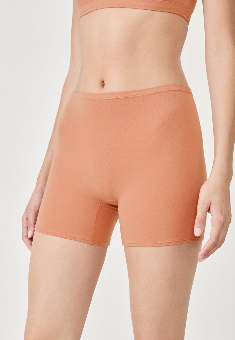Persikofärgade elastiska shorts med en slät yta, med en längd till midjan och en diskret sömdetalj längs midjebandet.