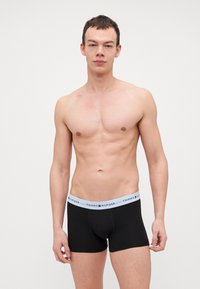 Schwarze Baumwoll-Boxershorts mit einem hellblauen Bund, der das Logo "TOMMY HILFIGER" trägt. Glatte Textur, enganliegendes Design und Oberschenkellänge.