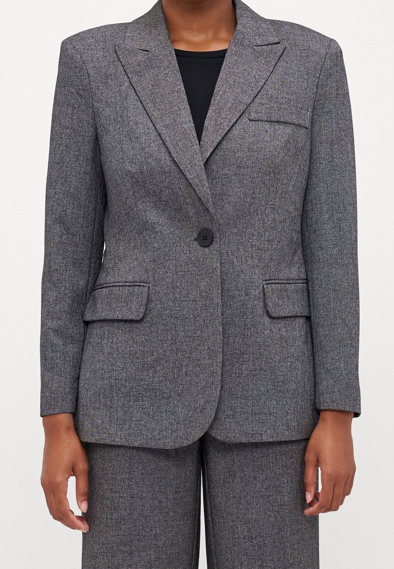 Grå texturerad blazer med en svart knapp, slagkrage, två framfickor och skräddarsydd passform. Matchas med en svart topp under.