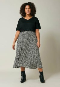 Zwarte V-hals T-shirt gecombineerd met een vloeiende, knielange rok met een zwart-wit stippenpatroon. Het model draagt zwarte hoge laarzen.