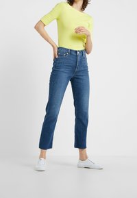 Högmidjade, raka blå jeans med en klassisk design med fem fickor, matchade med en kortärmad, klargul topp och vita sneakers.