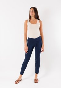 Top in beige chiaro abbinato a pantaloni aderenti blu navy. I pantaloni hanno una texture liscia e una silhouette moderna e slim. Sandali marrone senza chiusura.