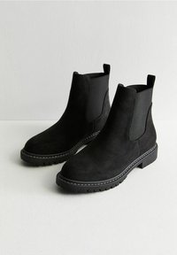 Czarne zamszowe botki Chelsea z elastycznymi panelami bocznymi, zaokrąglonym noskiem i teksturowaną gumową podeszwą. Charakteryzują się białym przeszyciem wzdłuż podeszwy.