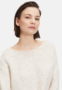 Strickpullover in Off-White mit lockerer Passform und weiter Ausschnitt. Besitzt einen strukturierten Stoff mit verstreuten metallischen Akzenten.