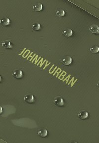Tessuto verde oliva con gocce d'acqua in rilievo e testo stampato "JOHNNY URBAN" in verde chiaro. Superficie testurizzata con una finitura opaca.