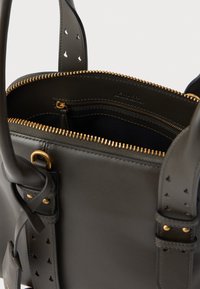 Bolsa de couro preto com detalhes em metal dourado, fecho com zíper e detalhes em tiras perfuradas. O interior inclui bolsos para organização.