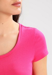 Camiseta de manga corta y escote redondo en tejido fucsia brillante, con una textura suave y costuras limpias.