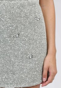 Jupe en tricot dans un motif gris clair et blanc, ornée d'accents floraux décoratifs avec des gemmes transparentes et des perles. Texture lisse.