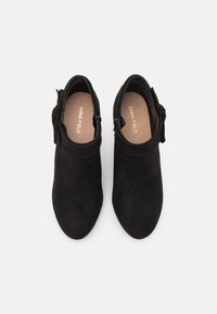 Stivali alla caviglia in suede nero con punta rotonda, zip laterali e fiocchetti decorativi al colletto, dotati di una fodera interna liscia.