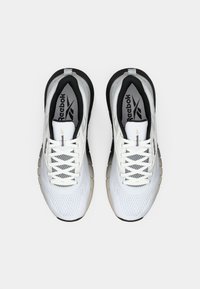 Adidași albi cu accente negre, partea superioară din plasă și talpă texturată. Prezintă șireturi albe și un logo gri pe limbă.