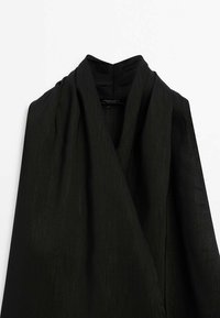Schwarzes Kleidungsstück mit einem Wickeldesign, ausgestattet mit einem glatten, strukturierten Stoff und einem hohen Kragen. Auffällig durch seine klaren Linien und minimalistischen Ästhetik.