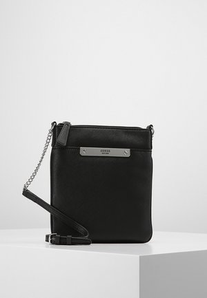 Schwarze Guess Umhängetasche aus Leder mit silberner Kettenriemen und Metall-Logoplate auf der Vorderseite, präsentiert auf weißem Podest.