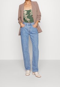 Krémový blazer, zelený květinový top, světle modré džíny s vysokým pasem a béžové mokasíny, zdůrazňující vrstvy, barvy a textury.