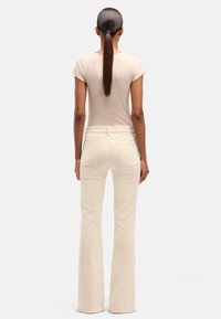 Beige tætsiddende t-shirt og cremefarvede udvidede jeans. Bomuldsblanding med en glat tekstur. Høj talje med baglommer og bæltestropper.