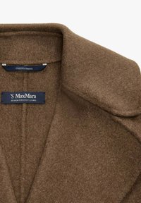 Collo di un cappotto marrone in lana con due etichette blu, una che recita "CUCITO A MANO" e l'altra "'S MaxMara DESIGN FOR EASY LIVING."