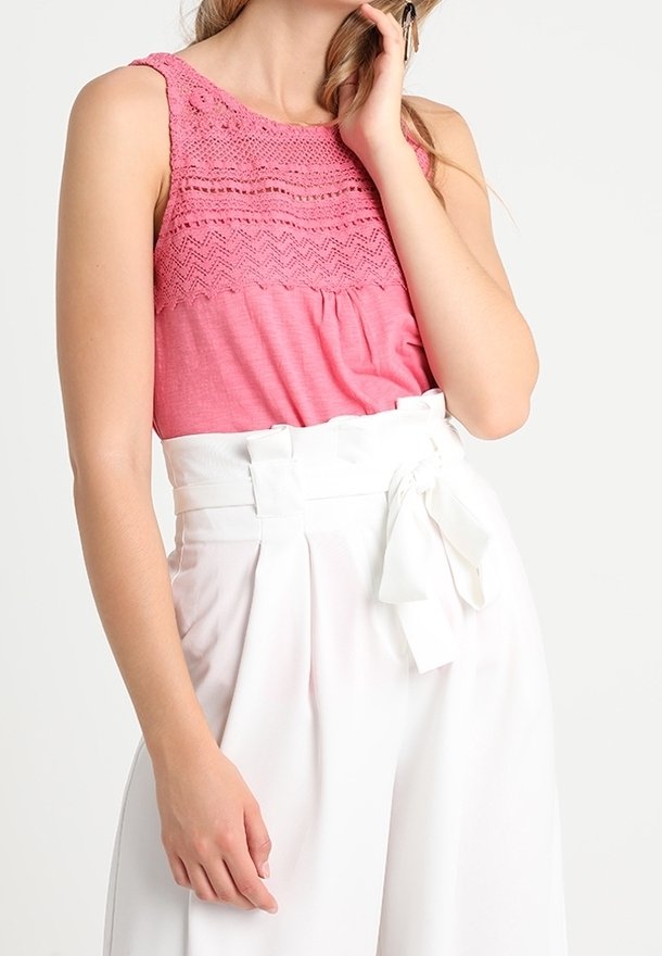 Lyserød ærmeløs top med tekstureret, hæklede halsudskæring og hvide højtaljede bukser med en bundet bælteDetalje.