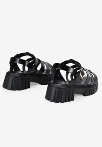 Sandali platform neri in pelle con più cinghie intrecciate e un tacco massiccio e rigato. Dettaglio a fibbia sul lato.