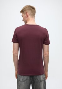 Burgundia lühikeste varrukatega t-särk, ümara kaelusega, sileda tekstuuriga, keha järgiva lõikega, sobitatud hallide teksapükstega, vaadatuna tagantpoolt.