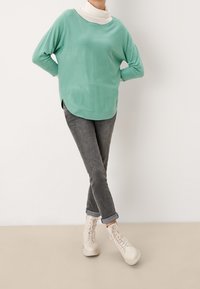 Pull surdimensionné vert menthe avec un ourlet arrondi, associé à un jean gris foncé retroussé et des bottines lacées couleur crème.